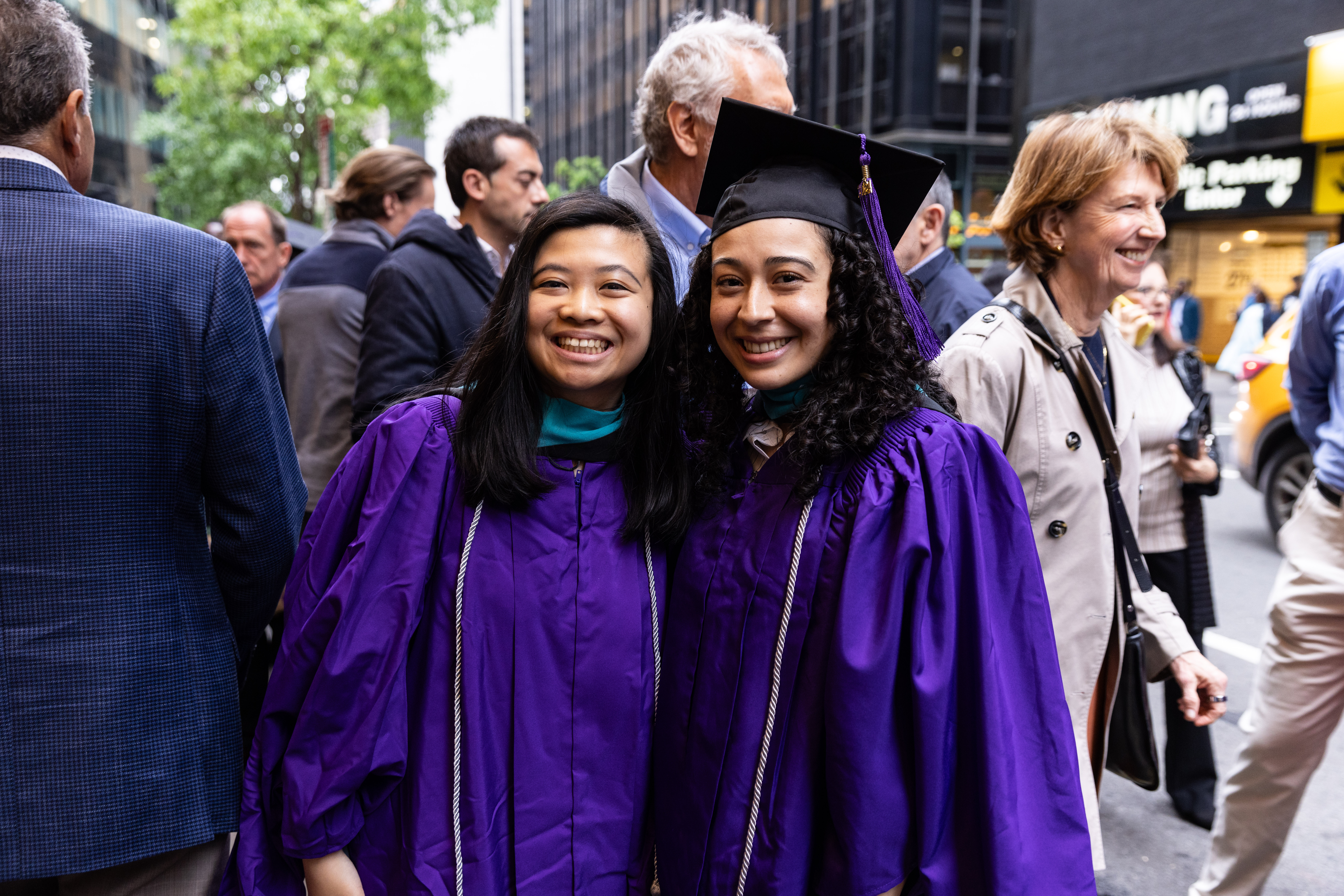 two students in purple graduation regalia standing in street smiling for camera