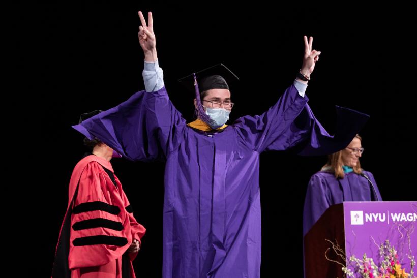Graduate walking across the stage and throwing two peace signs in the air