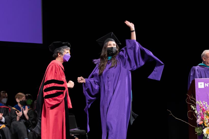 A graduate waving and walking across stage