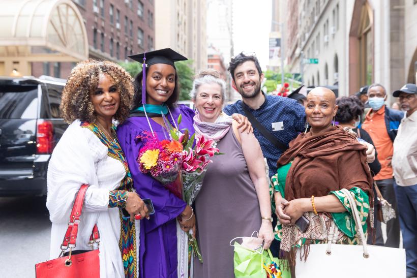 A graduate holding flowers with family members outside City Center