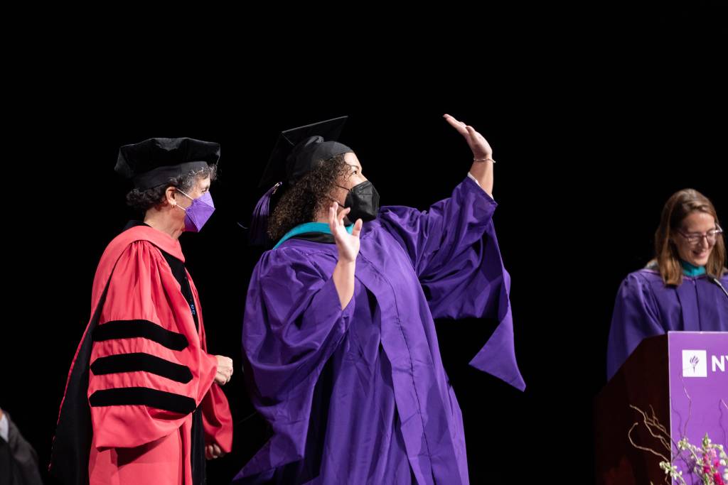Graduate waving to the audience on stage