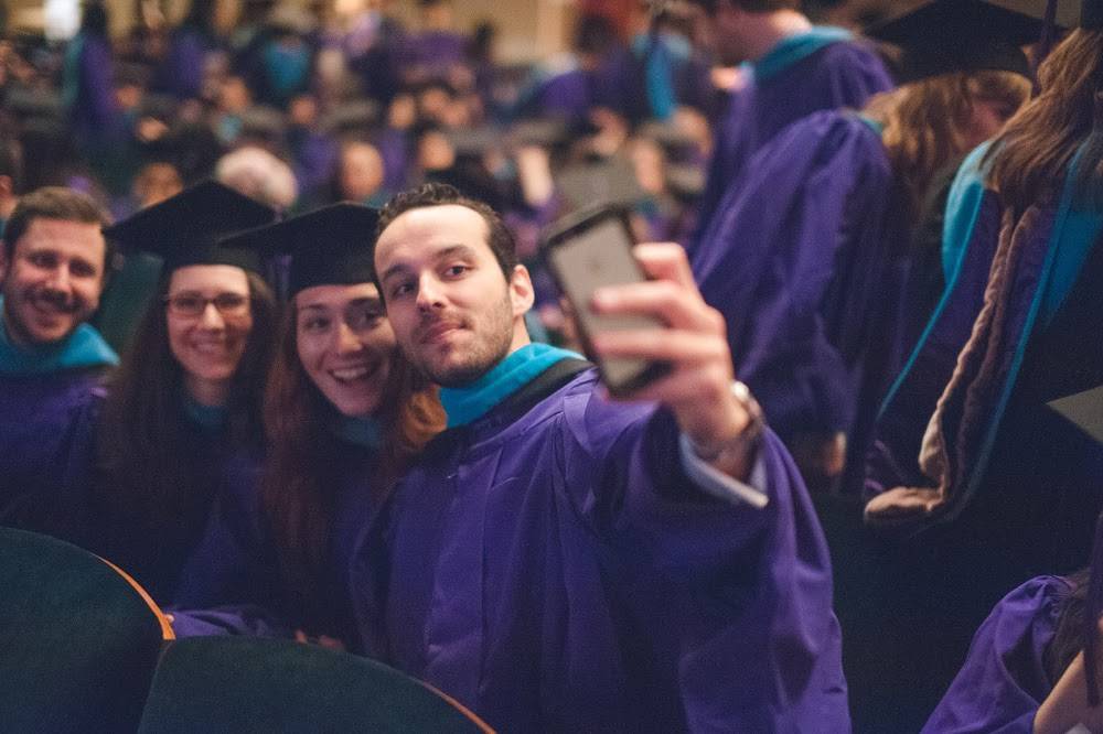 Students wearing graduation attire and taking a selfie