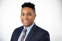 Pictured is a headshot of a young man in a suit. 
