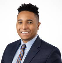Pictured is a headshot of a young man in a suit. 