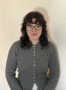 Pictured is a headshot of a young woman wearing glasses with medium length curly dark hair. 