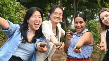 four students holding fruits and smiling