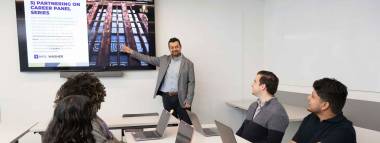 a person presenting in front of three students