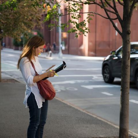 Person standing on street with notepad and pen in hand